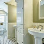 Remodeled bathroom with two pedestal sinks, tub toilet, black and white floor tile