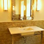 Pattern of floor and wall porcelain tile with variations of light brown colors in a bathroom with console lavatory, mirror and two sconces