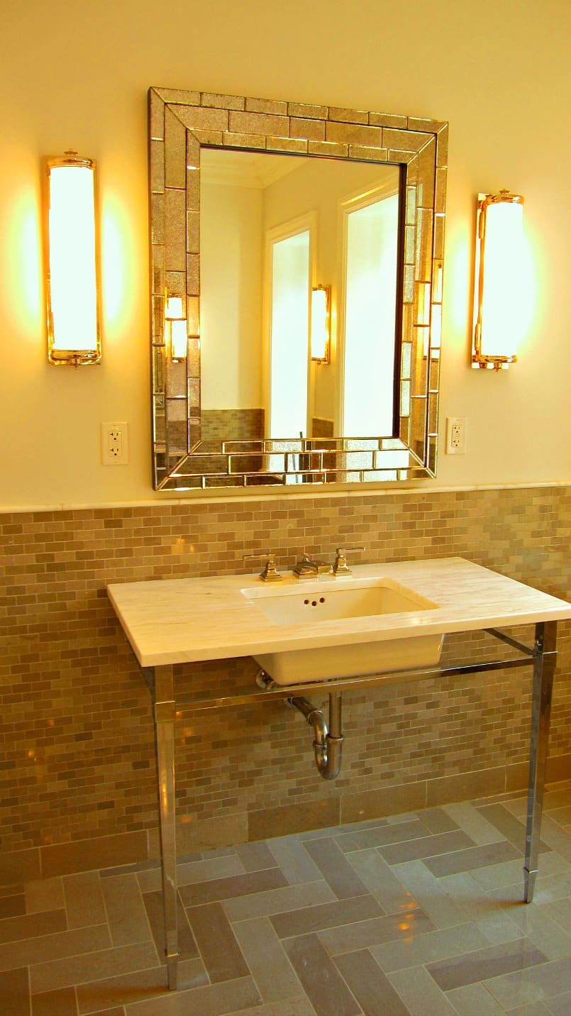 Pattern of floor and wall porcelain tile with variations of light brown colors in a bathroom with console lavatory, mirror and two sconces 