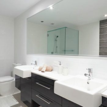 Double vanity with two white sinks mirror above and toilet beside