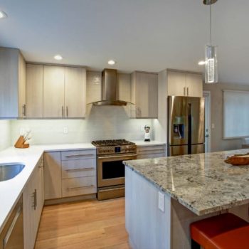 View of modern kitchen with island, counter lighting, tile backsplash and recessed lights.