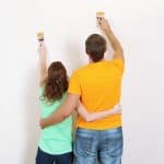 A couple with arms around one another while painting wall
