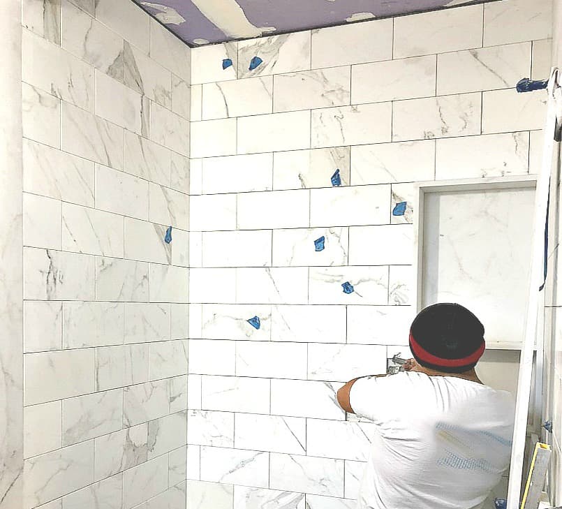 Worker Installing stone wall tile on bathroom shower wall