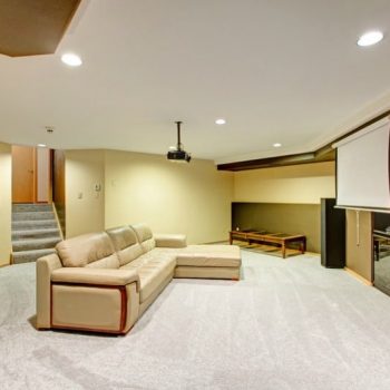 Basement media room with roll down screen and a couch lit by recessed lighting