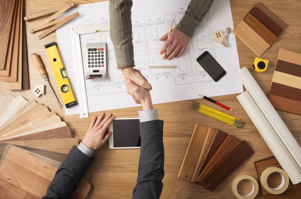 Handshake across a table top containing drawings, materials samples and tools