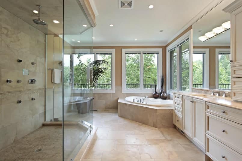 Large, complex renovated master bath with shower stall, frameless glass enclosure, beige floor tile, tub set into platform beneath windows and long vanity adjacent to the tub 